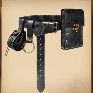 K&ouml;nnte beinhalten: Schwarzer Lederg&uuml;rtel mit angebrachten Taschen und einem rechteckigen Etui. Der G&uuml;rtel hat eine Schnalle, einen langen Riemen mit gleichm&auml;&szlig;ig verteilten Nieten und eine kleine runde Tasche mit Kordelzug. Das rechteckige Etui hat einen dekorativen Verschluss und ist mit Nieten verziert.