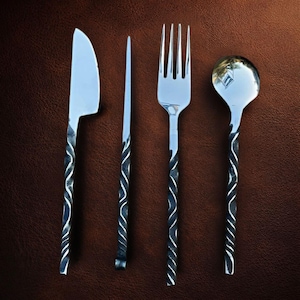 May include: A set of four stainless steel utensils: a knife, a butter knife, a fork, and a spoon. Each utensil has a twisted, dark metal handle. The knife has a curved blade, and the spoon has a round bowl.