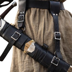 May include: Black leather sword scabbard with silver accents and a matching belt and shoulder straps. The scabbard is secured with adjustable straps and silver buckles. The sword handle is visible.