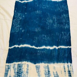 May include: A rectangular scarf featuring a tie-dye pattern in deep blue and white. The design consists of horizontal bands of solid blue alternating with white sections that display intricate, repeating chevron-like textures. The ends have fringe.