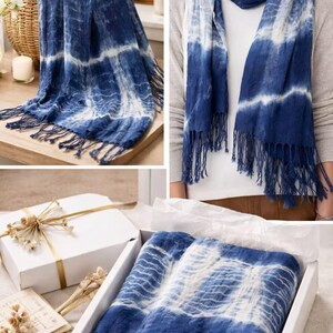 May include: A rectangular scarf featuring a deep blue and white tie-dye pattern with horizontal stripes and fringed edges. The fabric displays a textured appearance with varying shades of indigo and white, finished with long tassels on both ends.