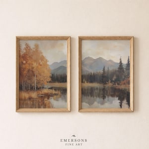 May include: Two framed landscape art prints featuring a mountain range, a calm lake, and a forest with autumn-toned foliage in shades of orange, brown, and muted green. The prints are housed in light-colored wooden frames. Text at the bottom reads EMERSONS FINE ART.