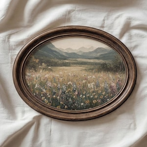 May include: An oval framed landscape painting. The artwork shows a field of wildflowers, with hills and mountains in the background. The frame is dark brown wood. The painting evokes a vintage aesthetic, suitable for home decor.