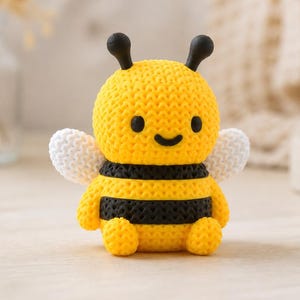 May include: A handcrafted, yellow and black bee figurine with white wings and black antennae. The bee has a smiling face and is made of a textured material. The figurine is a decorative item.