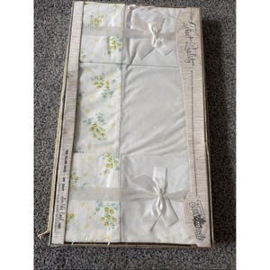 Puede incluir: Un juego de sábanas para cama doble en caja de Tex-made, etiquetado como Select Quality. El juego incluye dos fundas de almohada y una sábana, con tela blanca y un estampado floral amarillo y azul, decorado con cintas y lazos de satén.