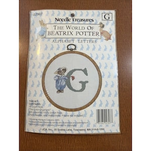 以下が含まれることがあります： Needle Treasures The World of Beatrix Potter クロスステッチキット、文字G用。パッケージには、青い服を着たキャラクターと文字Gが描かれた円形の刺繍枠のデザインが施されています。18カウントのアイーダ布とコットン刺繍糸が含まれています。
