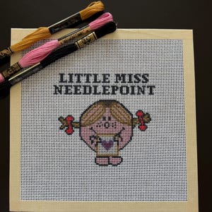 May include: Needlepoint canvas featuring a cartoon character with the text "LITTLE MISS NEEDLEPOINT". The canvas is surrounded by a beige border and has three spools of embroidery floss in gold, pink, and black.