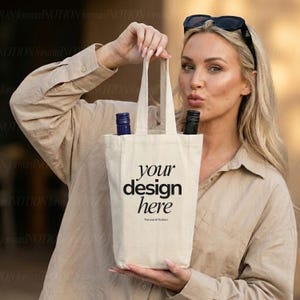 Puede incluir: Una bolsa de vino de lona beige con el texto "your design here" en negro. La bolsa contiene dos botellas de vino, una con tapón azul y otra con tapón negro. La bolsa es sostenida por una persona.