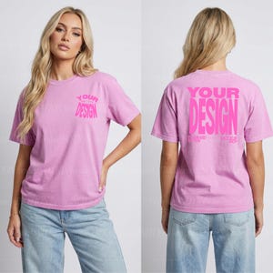 Puede incluir: Una camiseta de manga corta de color morado claro con cuello redondo. La parte delantera presenta el texto "YOUR DESIGN" en una fuente rosa más pequeña en el pecho izquierdo. La parte trasera muestra el mismo texto en una fuente rosa grande.