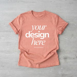May include: A coral-coloured t-shirt with rolled-up sleeves. The shirt features the text "your design here" in a white, bold font. The words "Forward Notion" are printed in a smaller font below the main text.
