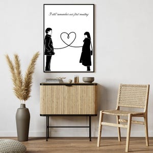 Pode incluir: Impressão artística emoldurada em preto e branco com duas figuras silhuetadas conectadas por uma linha em forma de coração. O texto "I still remember our first meeting" está acima. A obra de arte é exibida acima de um armário de madeira.