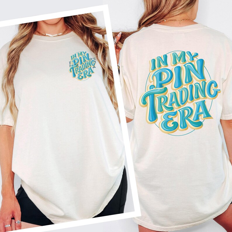 May include: An off-white t-shirt featuring a small graphic on the front left chest and a large matching graphic on the back. Both graphics display the text "IN MY PIN TRADING ERA" in a blue and yellow stylized font within a circular outline.