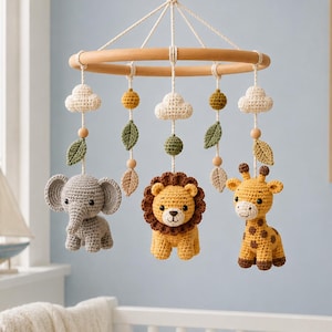 Può includere: Una giostrina sospesa per culla con una cornice circolare in legno e figure all'uncinetto di un elefante grigio, un leone marrone e giallo e una giraffa gialla. Include nuvole bianche lavorate all'uncinetto, foglie verdi e perline di legno.