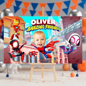 Peut inclure: Une impression sur toile personnalis&eacute;e avec le texte "OLIVER et ses AMAZING FRIENDS", repr&eacute;sentant des illustrations de Spider-Man, Iron Man et Spider-Gwen. L'&oelig;uvre comprend une photo d'un jeune enfant en tant que personnage central, sur fond de paysage urbain.