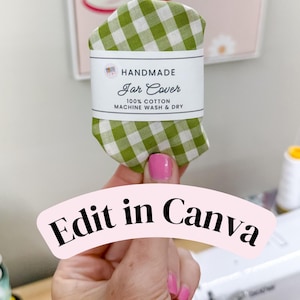 May include: A green and white gingham fabric jar cover wrapped in a white paper band. The band features the text HANDMADE Jar Cover 100% COTTON MACHINE WASH & DRY. The fabric is folded into a rounded shape with a visible checkered pattern.