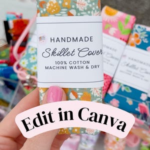 May include: A rectangular fabric skillet cover featuring a sage green background with a pattern of orange acorns, white leaves, and yellow flowers. A white paper label is wrapped around the center with the text HANDMADE Skillet Cover 100% COTTON MACHINE WASH & DRY.
