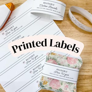 May include: A sheet of white paper with black printed labels for Reusable Cotton Rounds and Face Wipes, alongside two white paper bands and a stack of floral patterned fabric squares wrapped in a label reading Reusable Face Wipes.