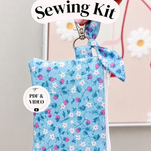 May include: A light blue fabric pouch with a floral and strawberry pattern, featuring a white zipper, a silver metal lobster clasp, and a knotted fabric tie. The pouch displays text reading Sewing Kit and PDF & VIDEO with a play icon.