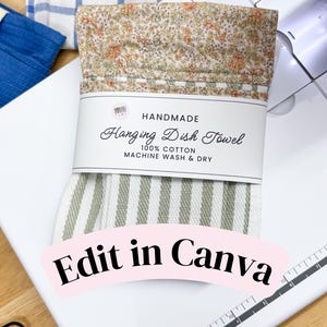 Puede incluir: Un paño de cocina colgante plegado con un patrón de rayas blancas y verde salvia en la parte inferior y un estampado floral en tonos melocotón y verde en la parte superior. Una etiqueta de papel blanca dice HANDMADE Hanging Dish Towel 100% COTTON.