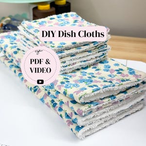 Könnte beinhalten: Ein Stapel DIY-Geschirrtücher mit einem blauen und lila Blumenmuster auf cremefarbenem Hintergrund. Die Tücher haben einen weißen, gefransten Rand. Auf dem Bild steht "DIY Dish Cloths" und "PDF & VIDEO".