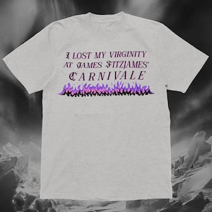 May include: A pale grey t-shirt featuring the text "I LOST MY VIRGINITY AT JAMES FITZJAMES' CARNIVALE" in purple and black. The design includes a graphic of purple and black flames beneath the text.