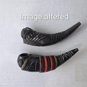 May include: Two dark brown, carved pipes. One pipe has detailed carvings and a decorative band. The other pipe has a band of red, orange, and white stripes. The text "Image altered" is in the background.