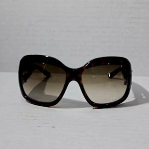 Può includere: Occhiali da sole marroni tartarugati con lenti sfumate. Le montature oversize hanno una forma arrotondata, leggermente a occhi di gatto. Le lenti passano da una tonalità più scura nella parte superiore a una più chiara nella parte inferiore.