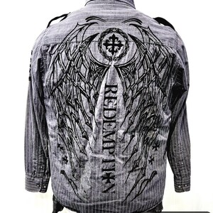 Könnte beinhalten: Grau gestreiftes Hemd mit schwarzem Grafikdesign auf dem Rücken. Das Design umfasst ein Kreuz, Flügel und das Wort "REDEMPTION". Das Hemd hat lange Ärmel und einen Button-Down-Kragen.