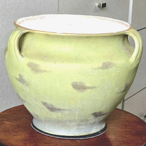 Puede incluir: Una maceta grande, redonda y verde de cerámica con dos asas. La maceta tiene una amplia abertura con interior blanco y borde marrón claro. Presenta formas abstractas de color marrón oscuro y se asienta sobre una base gris claro.