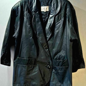 Puede incluir: Blazer de cuero negro con solapa de muesca, dos bolsillos delanteros y cierre de un solo botón. El blazer tiene mangas tres cuartos y una etiqueta que dice "Sonata".