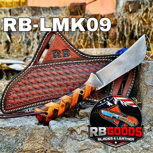 May include: A handcrafted knife with a wooden handle and a leather sheath. The knife blade is silver, and the handle features a brown and orange geometric design. The sheath is brown leather with a woven pattern and the text "RB-LMK09".