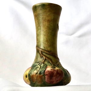 May include: A ceramic vase with a flared rim and a tapered neck, featuring a mottled olive green finish. The base is decorated with a raised, three-dimensional relief of brown branches, green leaves, and rounded fruit in shades of red and yellow.