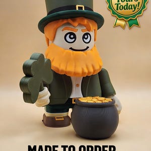 Könnte beinhalten: Eine große Leprechaun-Figur in Grün und Orange, die ein Kleeblatt und einen Goldtopf hält. Die Figur trägt einen grünen Zylinder und eine Jacke. Der Text auf dem Bild lautet "Get Yours Today!" und "MADE TO ORDER - STUDIO-GRADE PRINT."