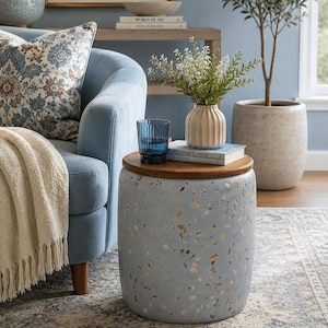 May include: A cylindrical side table featuring a light blue terrazzo base with embedded multi-colored stone fragments and a smooth, circular dark wood top. The table stands independently, providing a flat surface for decorative items.