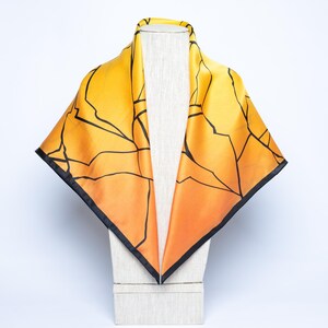 K&ouml;nnte beinhalten: Quadratisches Seidentuch mit einem Farbverlauf von Gelb zu Orange. Schwarze Linien bilden ein geometrisches Muster auf dem Tuch. Das Tuch hat einen schwarzen Rand und wird auf einem Mannequinkopf pr&auml;sentiert.