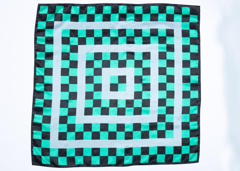 Op de afbeelding: Vierkante sjaal met een herhalend dambordpatroon in zwart en teal. Het ontwerp bevat concentrische vierkanten met afwisselende kleuren, waardoor een gedurfd en geometrisch visueel effect ontstaat. De sjaal is waarschijnlijk gemaakt van een lichte stof.