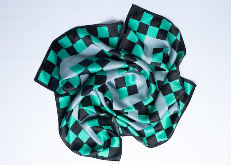 Op de afbeelding: Een vierkante sjaal met een geblokt patroon in zwart, teal en grijs. De sjaal is gemaakt van een zijdeachtig materiaal en is gedrapeerd op een witte ondergrond. Het ontwerp heeft een herhalend patroon van vierkanten.