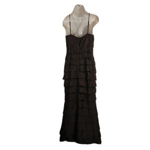 May include: A dark brown, floor-length dress with a tiered, ruffled design. The dress features thin spaghetti straps and a fitted bodice. The back of the dress is visible, showcasing the zipper closure. The dress is displayed on a mannequin.