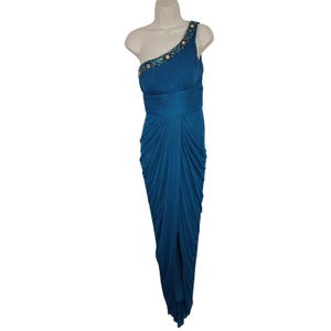 May include: Teal one-shoulder formal dress with a draped design. The dress features a fitted bodice with embellished shoulder detailing and a flowing skirt. The dress is displayed on a mannequin.