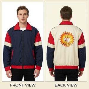 May include: A zip-up jacket featuring a navy blue front with red and cream accents, a red collar, and a red waistband. The back is cream-colored with red and navy sleeves, displaying a sun graphic with theater masks and the text MWR ENTERTAINMENT PROUD+LOUS.