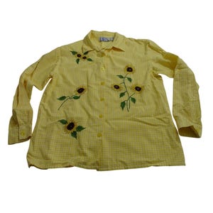 Op de afbeelding: Een gele button-down shirt met een ruitpatroon en geborduurde zonnebloemen. De lange mouwen shirt heeft een kraag en gele knopen. De merknaam "BEA" is op de kraag geborduurd. Een vrolijk, zomers kledingstuk.