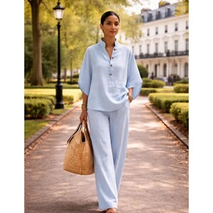 May include: A light blue linen two-piece outfit, consisting of a short-sleeved top with wooden buttons and matching wide-leg pants. The outfit is paired with a woven straw tote bag and gold bracelets. The ensemble is suitable for warm weather.
