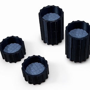 May include: Four black cylindrical objects with a textured interior and a ridged exterior. The objects are arranged on a white surface. The interior has a cross-hatched pattern.