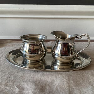 May include: A set of three ceramic mugs with a speckled, matte finish. The mugs are in shades of cream, light gray, and dark gray. Each mug has a simple, minimalist design and a rounded handle.