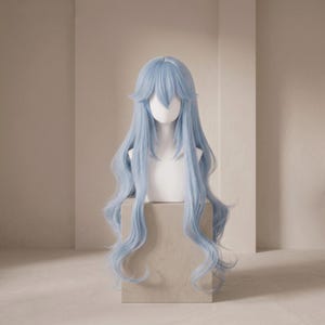 May include: A long, pale blue wig with wavy, layered hair. The wig is displayed on a white mannequin head and rests on a small, square, beige plinth. The wig has a fringe and long, flowing locks.