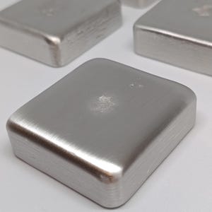May include: A collection of small, square, silver metal objects. Each has rounded corners and a brushed finish. The objects are arranged on a light surface, with one in sharp focus, showing the texture.