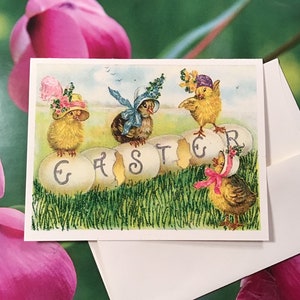 May include: A vintage Easter card featuring four chicks wearing hats and sitting on cracked eggs that spell out "EASTER". The chicks are yellow with brown wings and have pink, blue, and purple hats. The background is green grass with glitter.