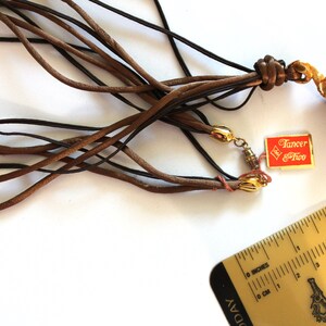May include: A brown leather cord necklace with a gold rose pendant and a tag that reads "Tancer & Two".