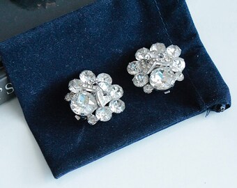 Può includere: Un paio di orecchini in tono argento con grappoli di strass trasparenti. Gli orecchini sono su uno sfondo di velluto blu scuro.