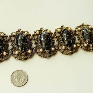May include: A gold tone bracelet with five oval black and white cameo-like stones set in ornate filigree. The bracelet is accented with small white faux pearls.